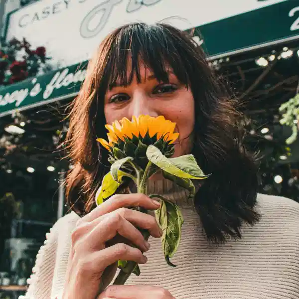 Femme souriante avec un tournesol illustrant le mieux-être après un accompagnement pour l'anxiété