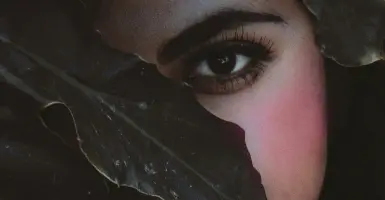 Femme se cachant le visage dans des fleurs roses, illustrant la honte et la peur de rougir