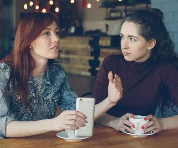 Deux femmes en conversation dans un café, l'une écoute attentivement l'autre qui s'exprime