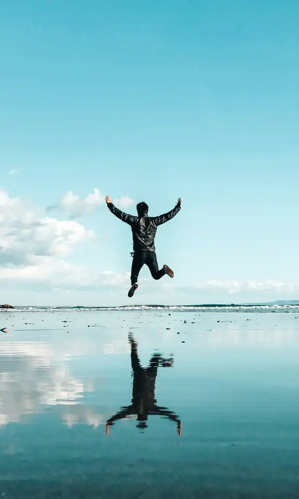 Silhouette en saut sur une plage, bras ouverts, reflet dans l'eau