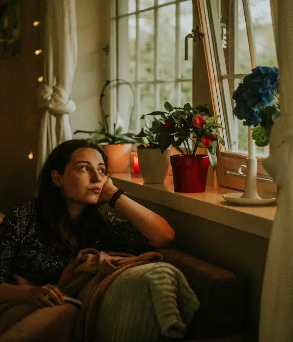 Femme assise pensive près d'une fenêtre, illustrant le quotidien de quelqu'un qui cherche à calmer son anxiété
